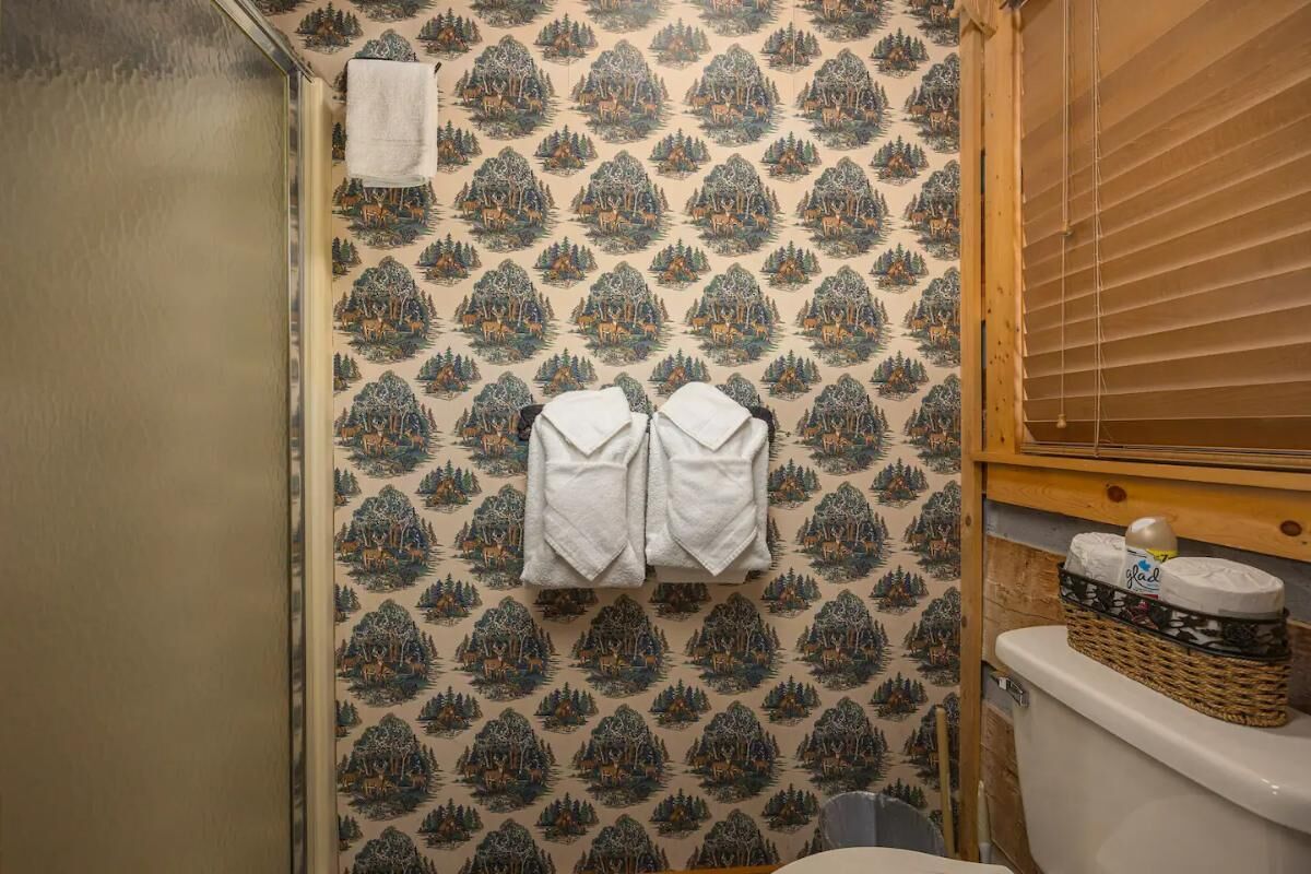 A bathroom with patterned wallpaper, a toilet, a sink, and a towel rack with two towels.