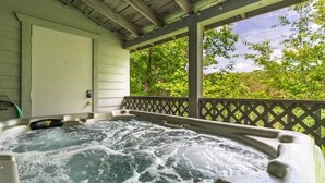A hot tub under a covered porch with a view of trees. - Tiny Pines (Sevierville)