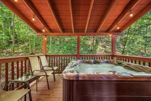 A hot tub on a wooden deck with chairs, surrounded by a forest. - Friends in High Places 2 (Sevierville)