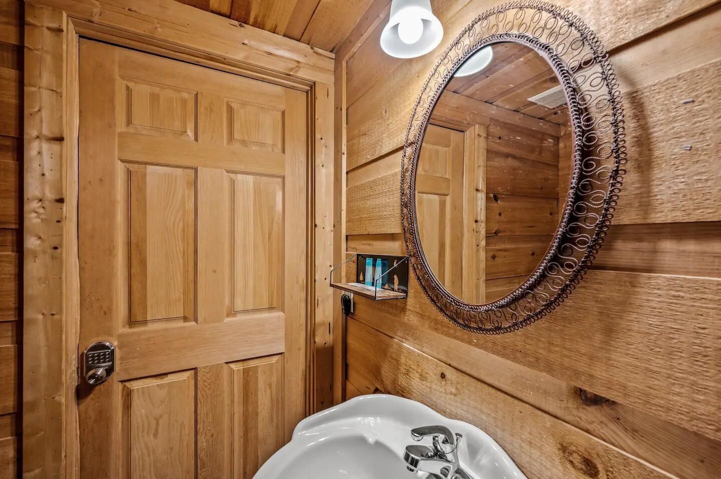A wooden bathroom with a door, a mirror, and a sink.