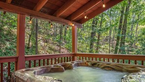 Un jacuzzi bajo una terraza de madera, con un bosque de fondo.