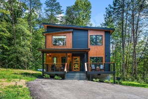 Ein modernes, zweistöckiges Haus mit einer hölzernen Veranda, großen Fenstern und einem Balkon.