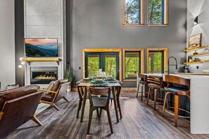 Ein modernes Interieur mit Kamin, Essbereich, Bar und großen Fenstern.