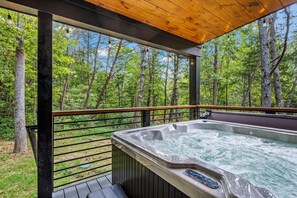 Ein Whirlpool auf einer Holzdielen-Terrasse mit Blick auf einen Wald.