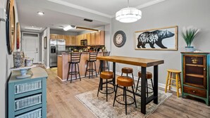 A modern kitchen with wooden cabinets, a central island with stools, a dining table, and a bar area with stools. - River Overlook (Sevierville)