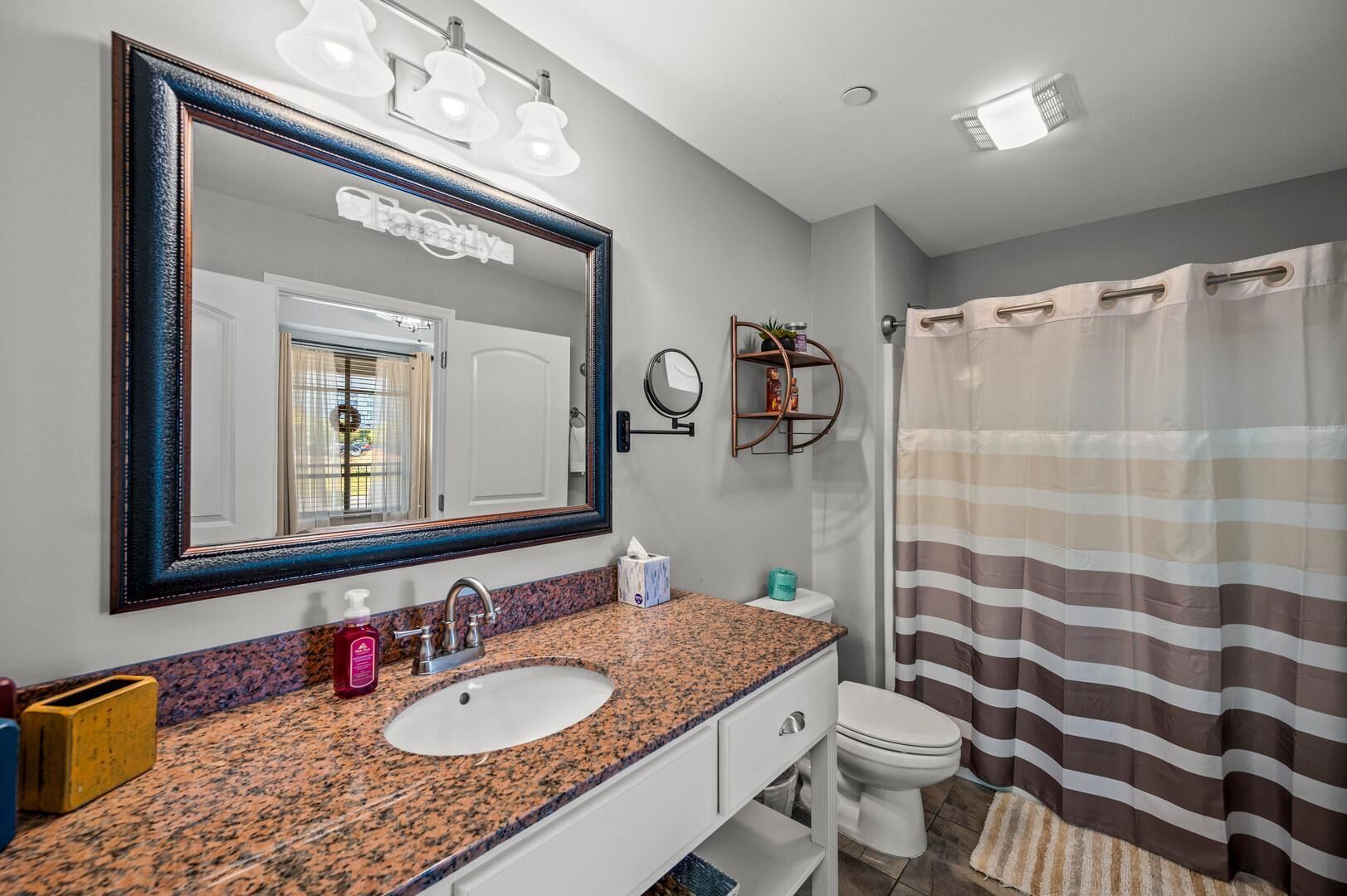 Un bagno con lavabo su piano in granito, uno specchio grande, un portasciugamani e una tenda da doccia a righe.