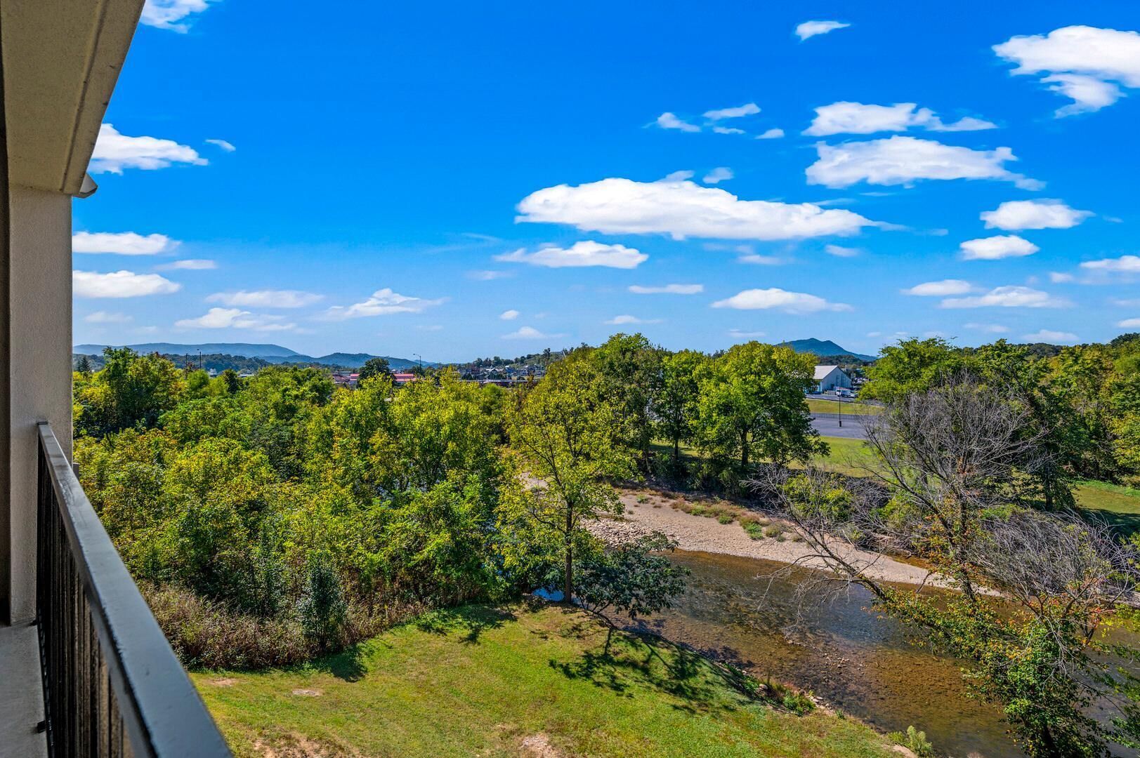 A balcony with a view of a river, trees, and distant mountains.