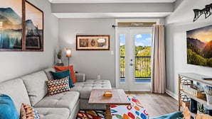 A living room with a sofa, a coffee table, and a TV. There is a door leading to a balcony with a view of greenery. - River Overlook (Sevierville)