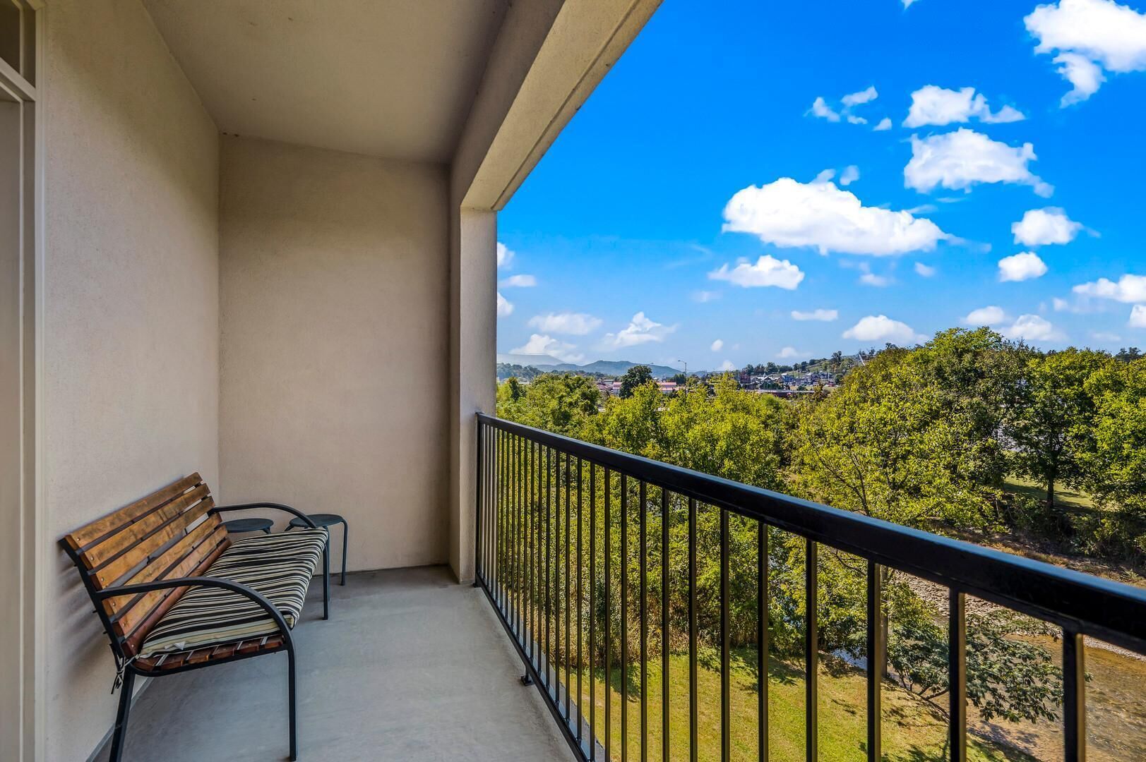 Ein Balkon mit Bank, Geländer und Blick auf eine grüne Landschaft mit Bäumen und einer in der Ferne liegenden Stadt.
