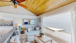 Ein geräumiger Wohnbereich mit Holzboden, einem großen Fenster mit Aussicht, einer Couch, einem Couchtisch und einem Deckenventilator.