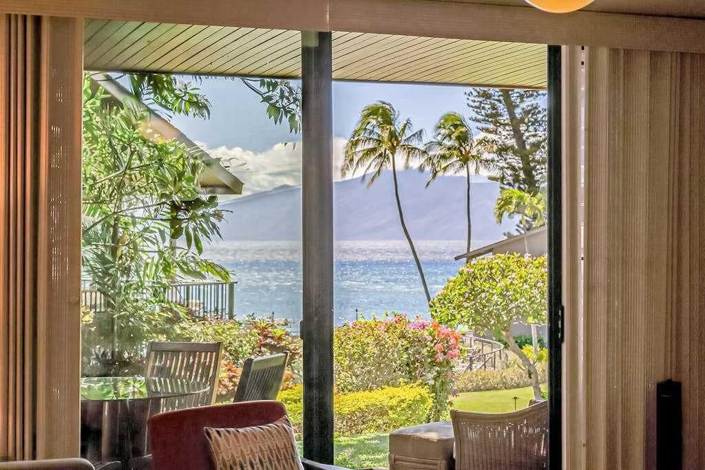 Una habitación con un gran ventanal corredero que da a vistas del océano y palmeras.