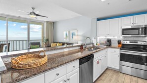 A modern kitchen with white cabinets, a granite countertop, stainless steel appliances, and a view of the ocean. - Majestic View Oceanfront (Panama City Beach)