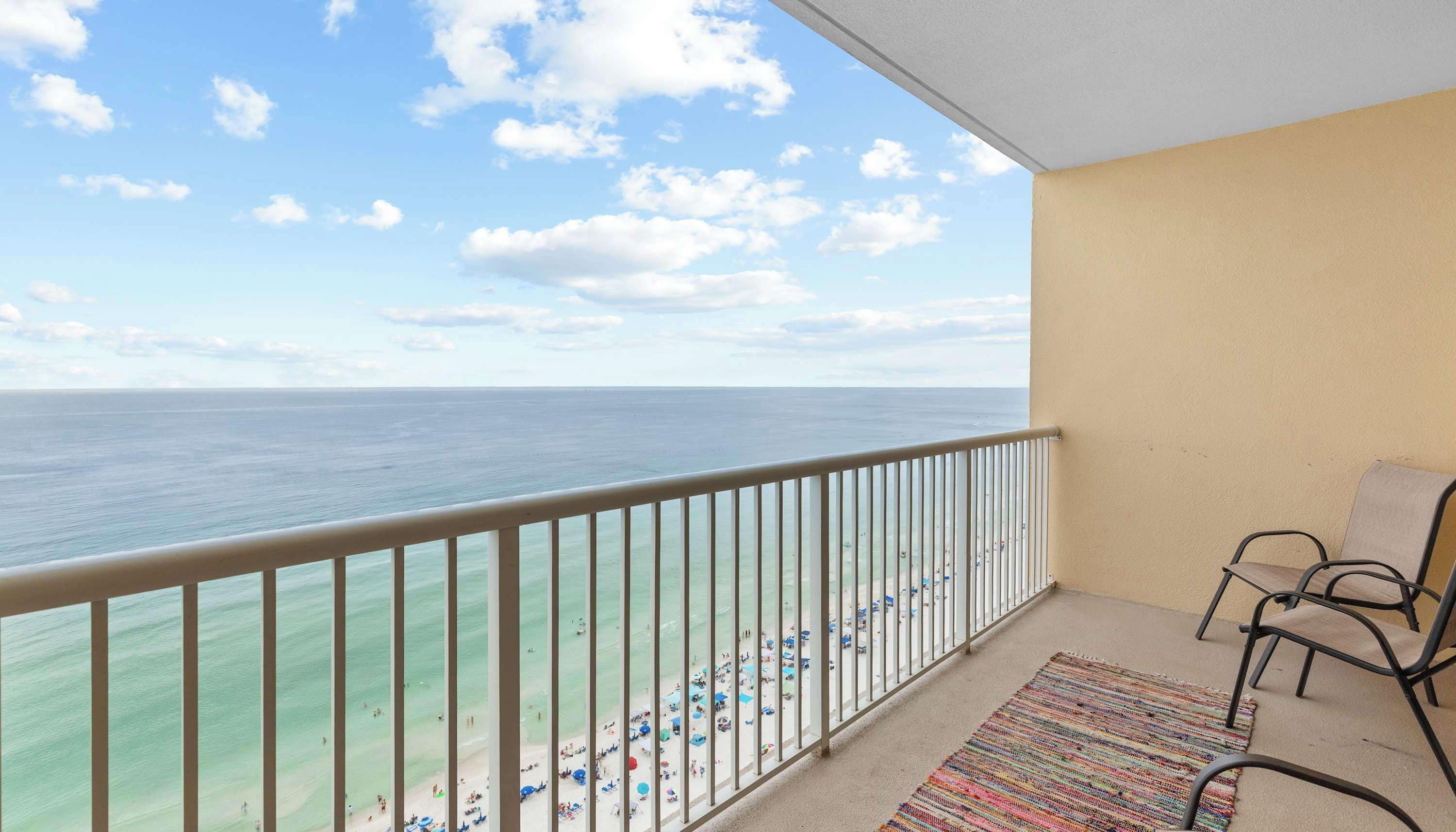 A balcony with a view of the ocean, a chair, and a colorful rug.