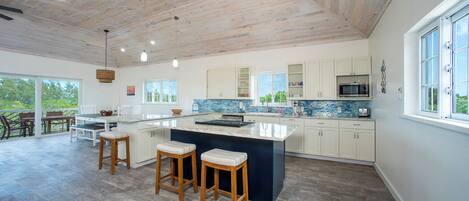Cocina moderna con una isla grande, armarios blancos y vistas al exterior.