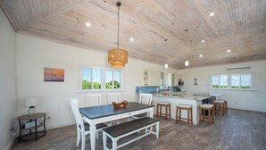 Una cocina amplia con comedor, techo de madera y ventanas grandes.
