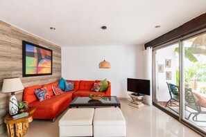 A modern living room with a red sofa, white ottoman, and a television. - A house with 2 bedrooms, 2 bathrooms, and a half-bath, featuring a large pool area! (Cancún)