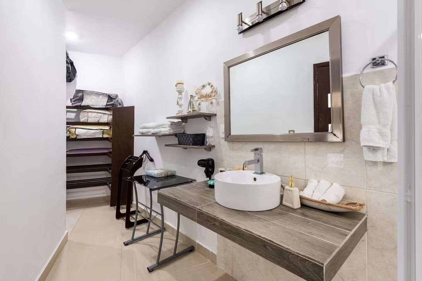 A bathroom with a round sink, a mirror, a towel rack, and a shelf with folded towels.