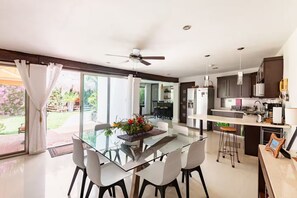 A modern kitchen with a glass dining table, white chairs, and a ceiling fan. - A house with 2 bedrooms, 2 bathrooms, and a half-bath, featuring a large pool area! (Cancún)