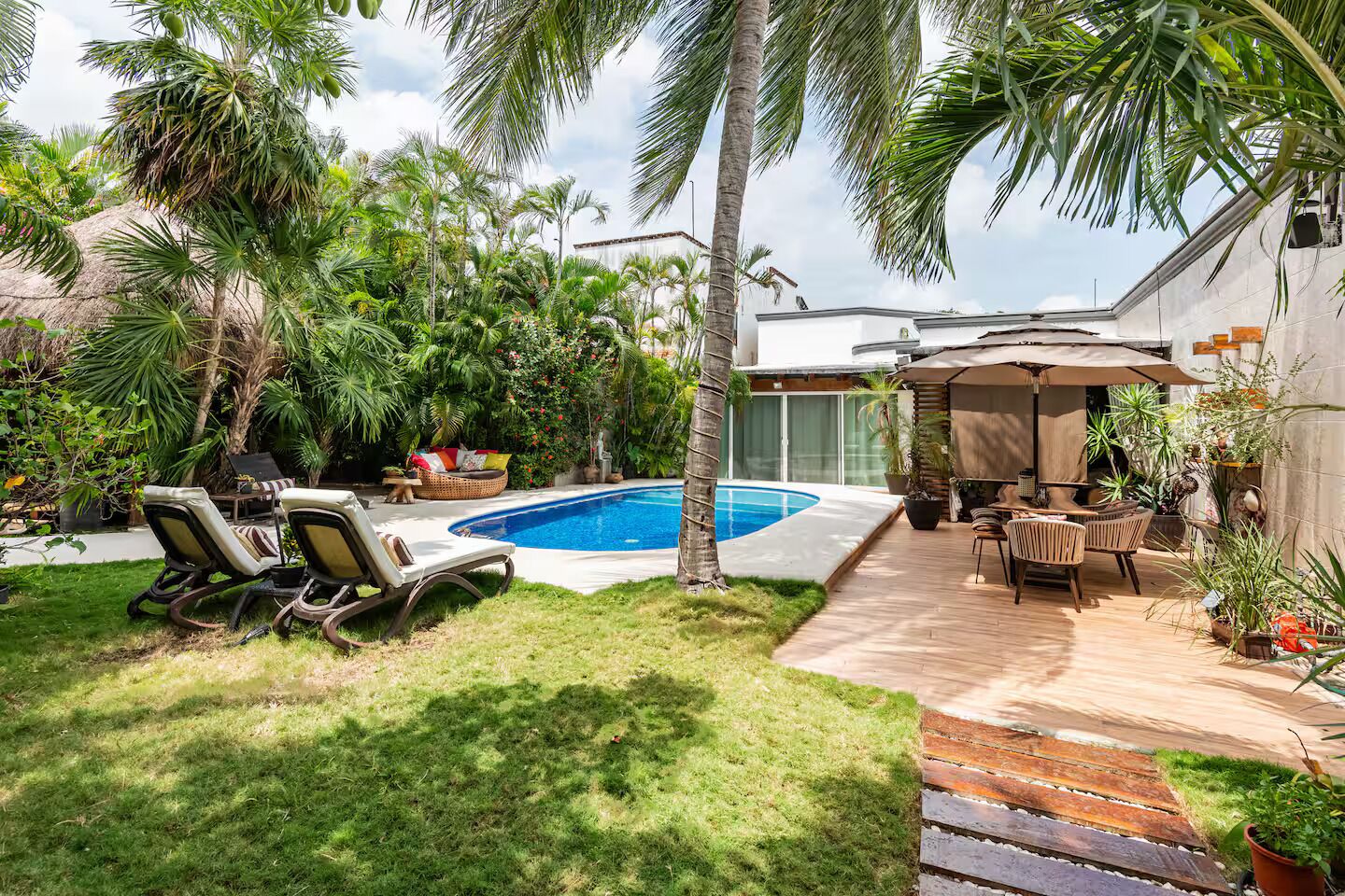 A backyard with a swimming pool, lounge chairs, a wooden deck, and various potted plants.