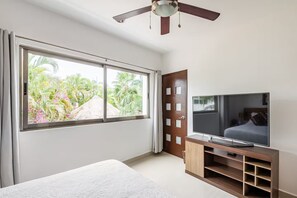 A bedroom with a large window, a ceiling fan, a TV, and a bed. - A house with 2 bedrooms, 2 bathrooms, and a half-bath, featuring a large pool area! (Cancún)