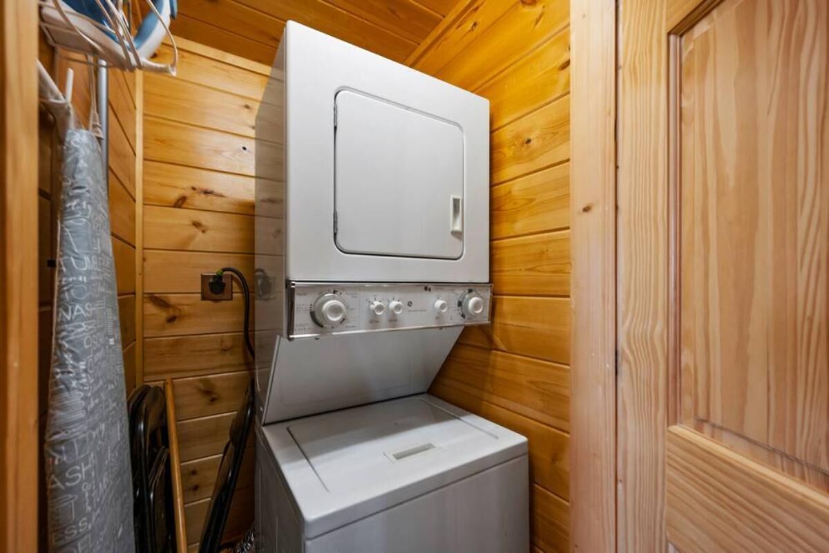 A compact laundry room with a washing machine and dryer, wooden walls, and a door.