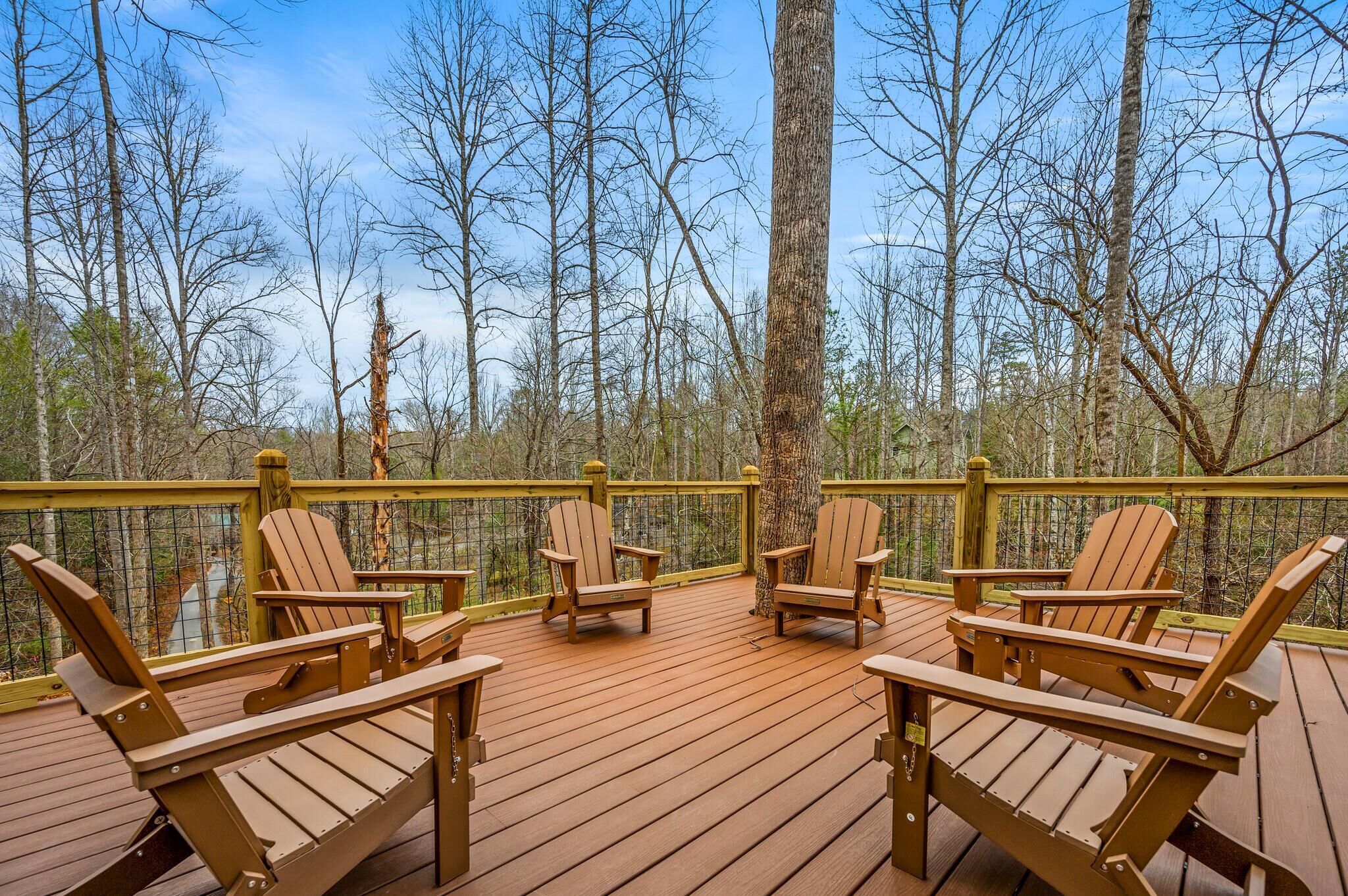 A wooden deck with Adirondack chairs, surrounded by trees.