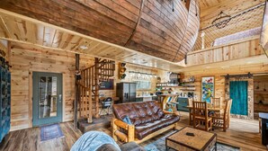 A wooden cabin interior with a sofa, dining table, and chairs, a kitchen area, and a staircase. - Neverland (Gatlinburg)