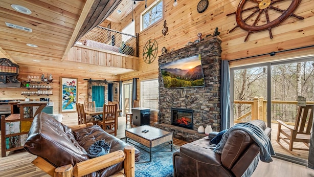 A spacious wooden interior with a fireplace, leather seating, and a balcony overlooking trees. - Neverland (Gatlinburg)