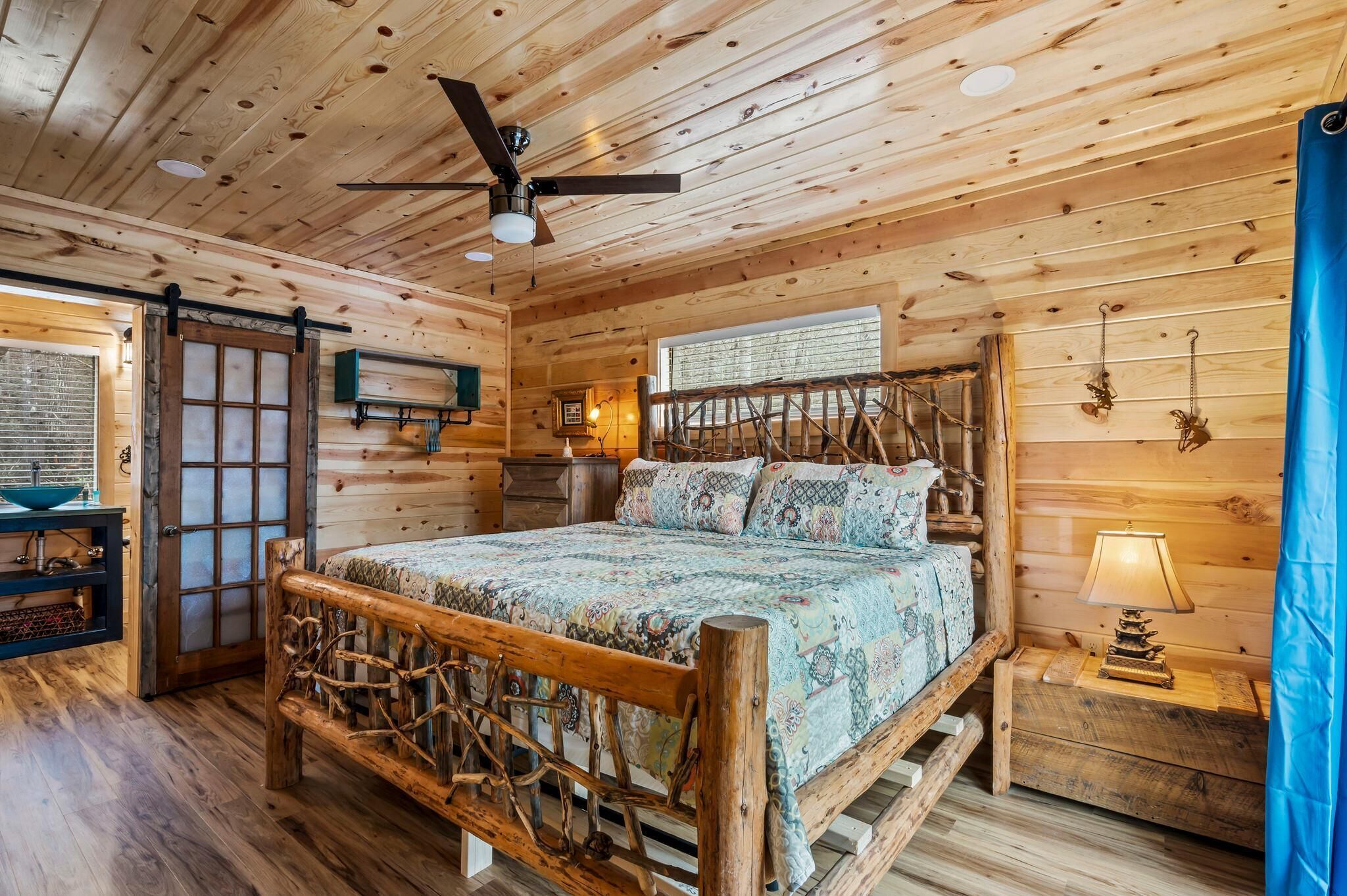 Ein Schlafzimmer in einer Holzhütte mit einem Bett, einem Deckenventilator, einem Fenster und einem Nachttisch.