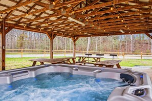 A wooden gazebo with a hot tub, picnic tables, and a view of a forest. - A Family Tradition (Gatlinburg)