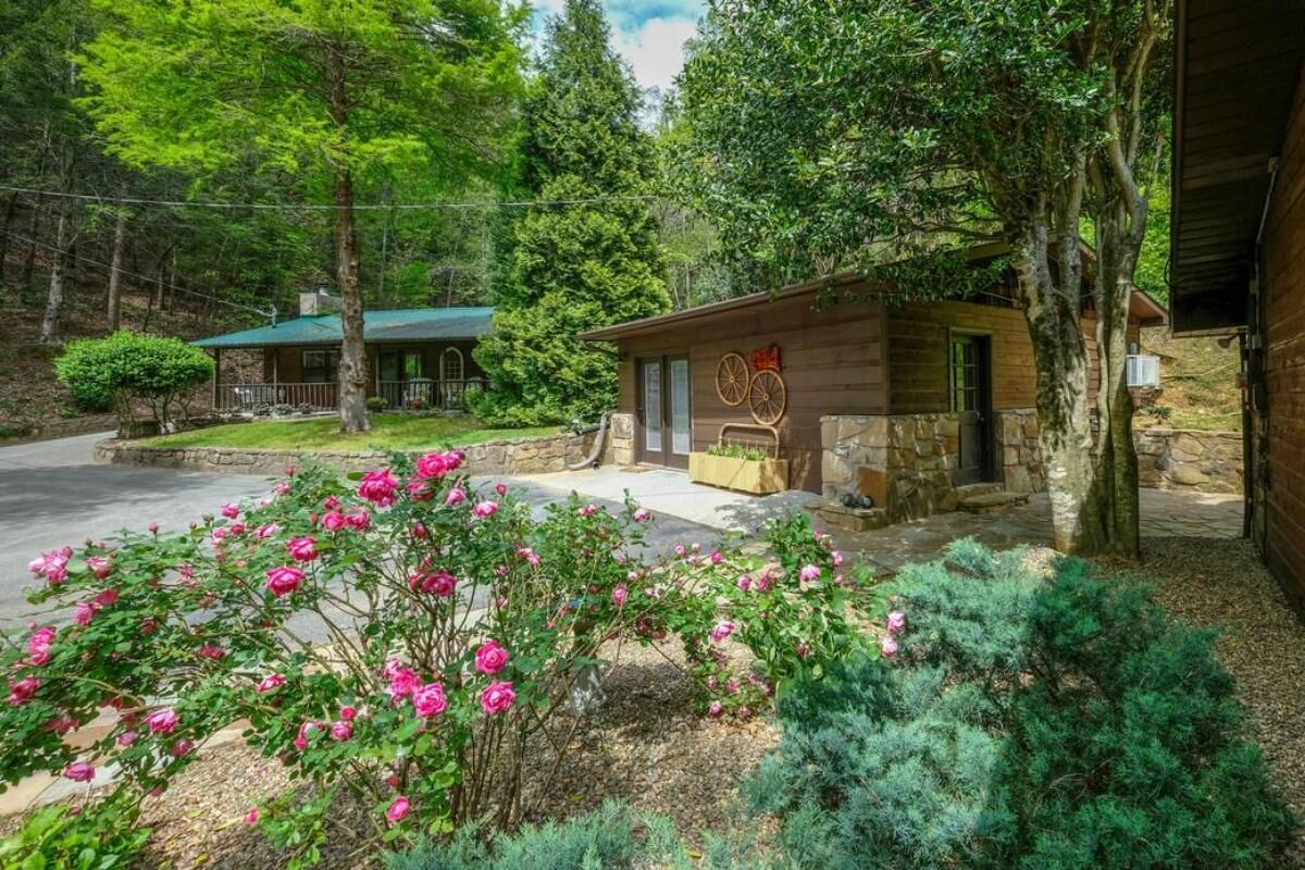 A rustic cabin with a stone exterior, a wooden porch, and a garden with pink flowers.