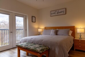 A bedroom with a bed, bench, bedside tables, and a balcony door. - Cozy Vista Condo (Pigeon Forge)