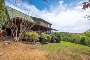 A wooden cabin with a green roof, surrounded by a grassy area and trees. - Fox n' Socks (Sevierville)