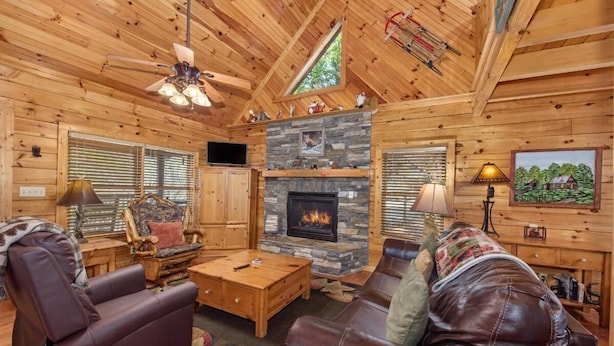 A log cabin interior with a stone fireplace, leather furniture, and a television. - Fox n' Socks (Sevierville)