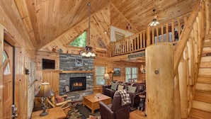 A log cabin interior with a stone fireplace, wooden furniture, and a balcony. - Fox n' Socks (Sevierville)