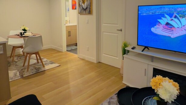 Una sala de estar con televisor, un sofá, un comedor con sillas y una cocina al fondo.