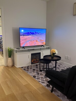 Ett modernt vardagsrum med en platt-TV, en öppen spis, en soffa och ett soffbord.