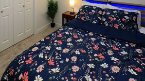 Un dormitorio con cama, mesita de noche, lámpara, ventana con persianas, luz de techo y armario.