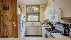 A compact kitchen with wooden cabinets, a refrigerator, a microwave, a stove, and a window providing natural light. - Enjoy stunning view in Waterville Estates! (Thornton)