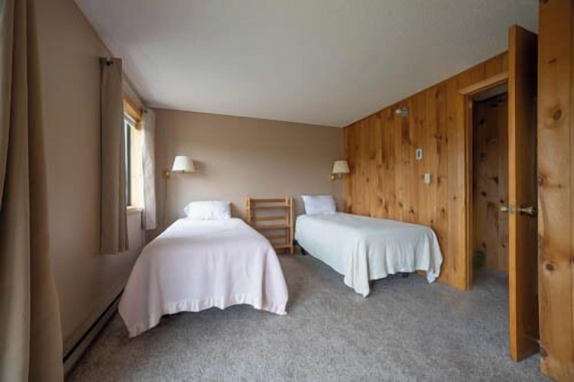 A room with two beds, wooden walls, a door, and a window.