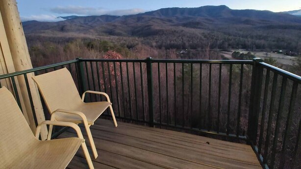 Un terrazzo in legno con due sedie, una ringhiera e vista sulle montagne.
