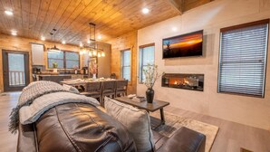 A cozy living room with a leather sofa, a fireplace, and a dining area with a kitchen in the background. - Hillside Horizon (Sevierville)