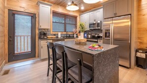 A modern kitchen with wooden walls, a central island, bar stools, and stainless steel appliances. - Hillside Horizon (Sevierville)