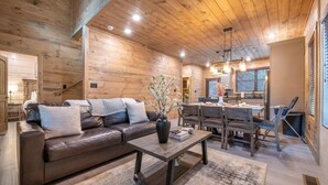 A cozy living room with a leather sofa, a coffee table, and a dining area with wooden furniture. - Hillside Horizon (Sevierville)