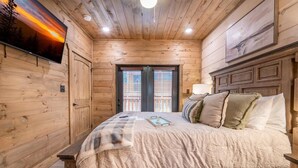 A wooden cabin bedroom with a bed, a TV, and a window with blinds. - Hillside Horizon (Sevierville)