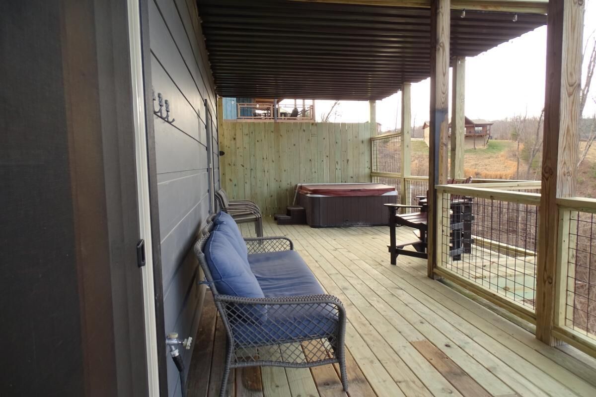 En inglasad veranda med flätade loungestolar, ett bubbelbad och utsikt över en inhägnad trädgård.