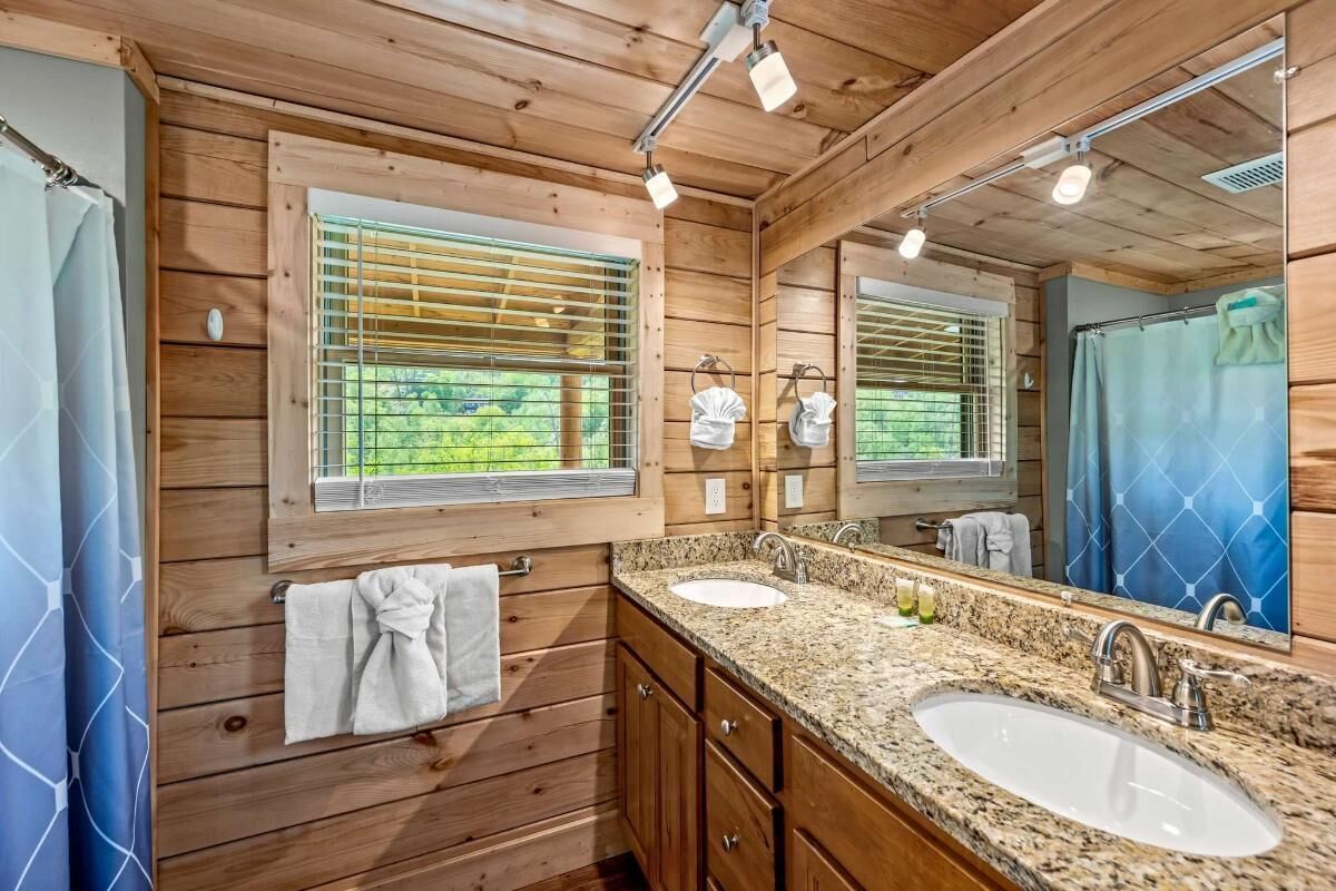 Ein Badezimmer einer Holzhütte mit zwei Waschbecken, einem großen Spiegel und einem Fenster mit Jalousien.
