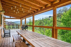 A wooden deck with picnic tables and chairs, overlooking a forested area with a view of distant buildings. - Rustic Retreat (Gatlinburg)