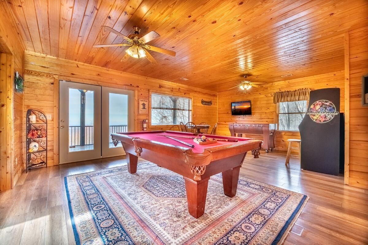 A wooden interior with a pool table, ceiling fans, and a television.