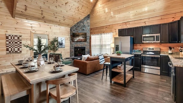 A spacious kitchen with modern appliances, a dining area with wooden furniture, and a cozy living space with a fireplace. - Lykke Lodge (Pigeon Forge)